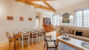 Un comedor con mesa y sillas de madera, un sofá y una escalera que sube a otro nivel.