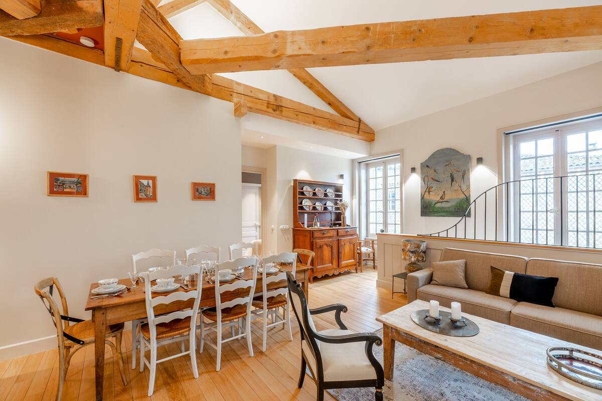 Un espace repas comprenant une table et des chaises en bois, un canapé et un escalier menant à un autre niveau.