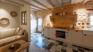 Una cocina con pared de piedra, vigas de madera, encimera blanca y horno empotrado.