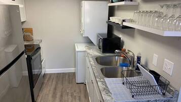 Cocina compacta con refrigerador, microondas, lavaplatos y lavadero pequeño.