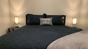 A bed with a dark quilt and a light blanket, two bedside lamps, and a pillow with the text "happy place".