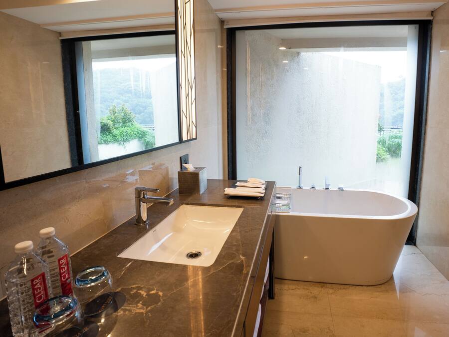 Een moderne badkamer met een grote wastafel, een badkuip en een groot raam met uitzicht op groen.