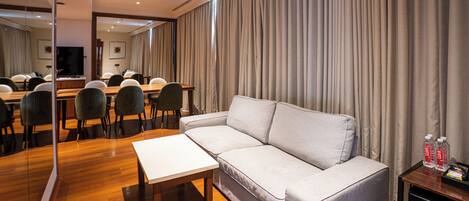 Une chambre d’hôtel moderne équipée d’un canapé, d’une petite table, d’un bureau avec des chaises, d’une télévision et d’un miroir.