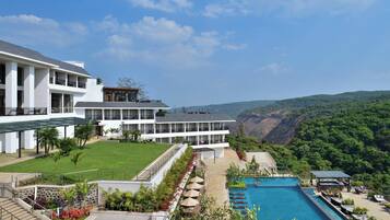 Relax by the rectangular pool surrounded by lounge chairs and umbrellas, with a scenic view of lush greenery and hills.