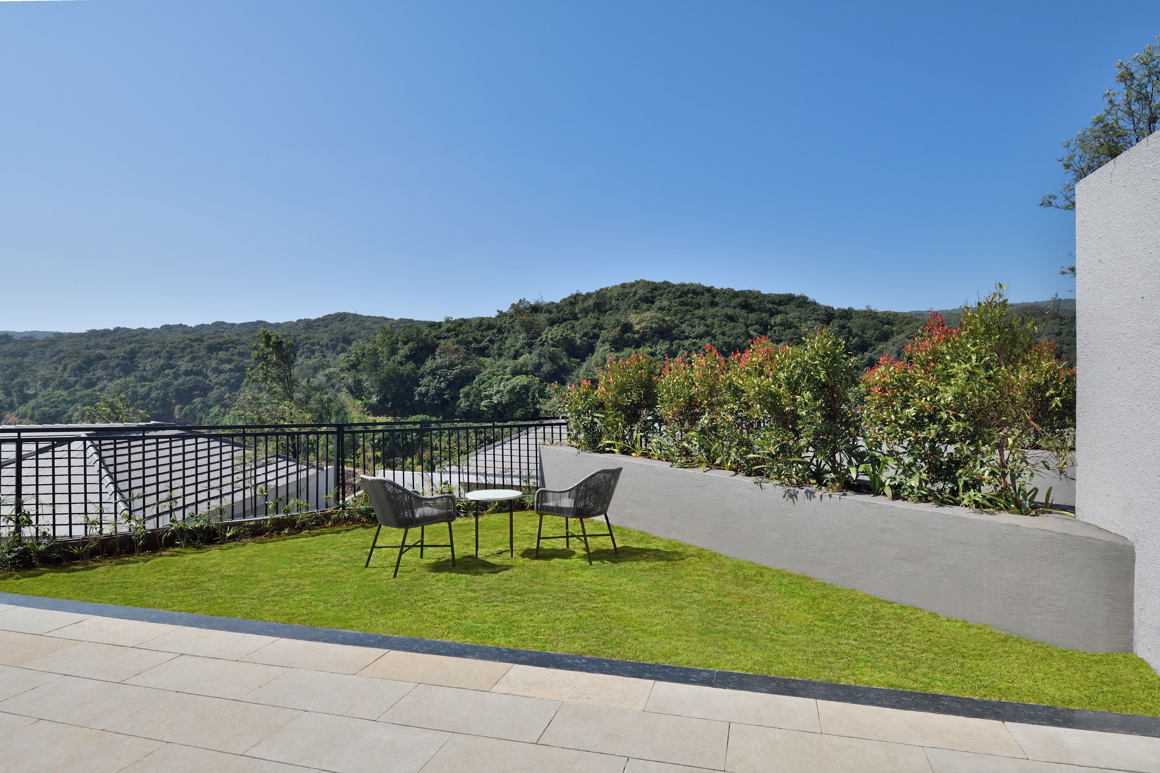 A terrace with a view of a forested hill, a pool, and two chairs.