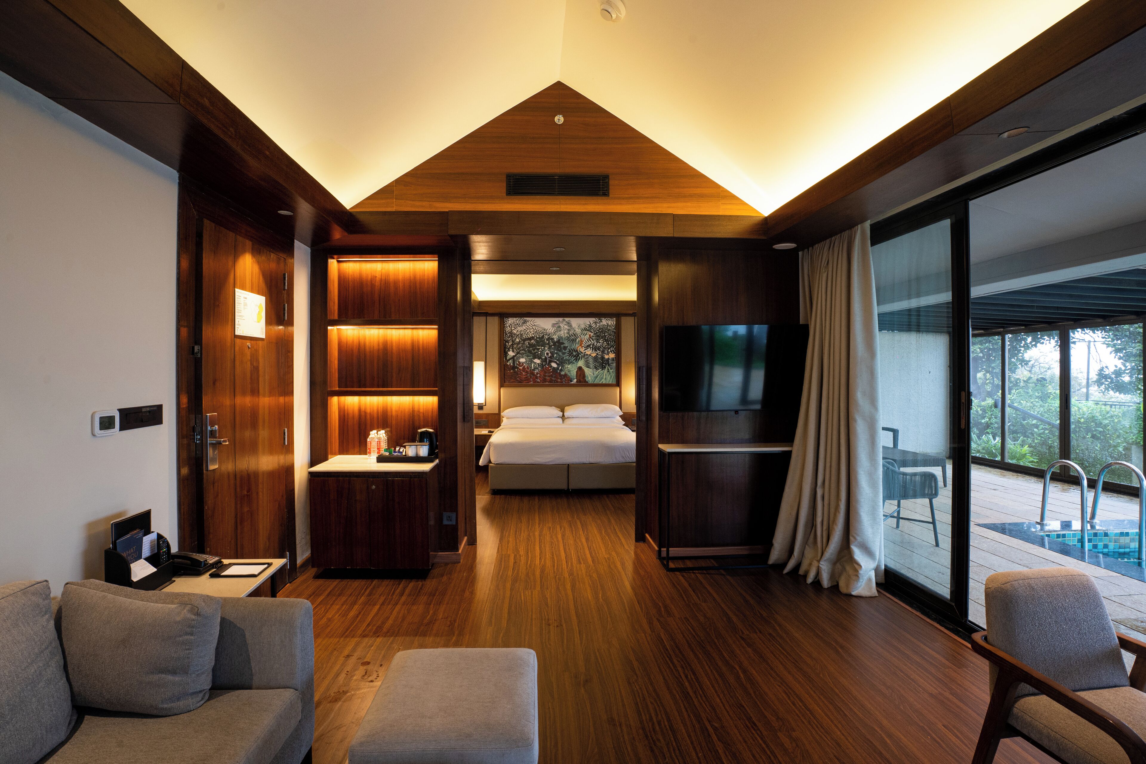 Una habitación de hotel moderna con piso de madera, una cama, un televisor, un escritorio y un balcón con piscina.