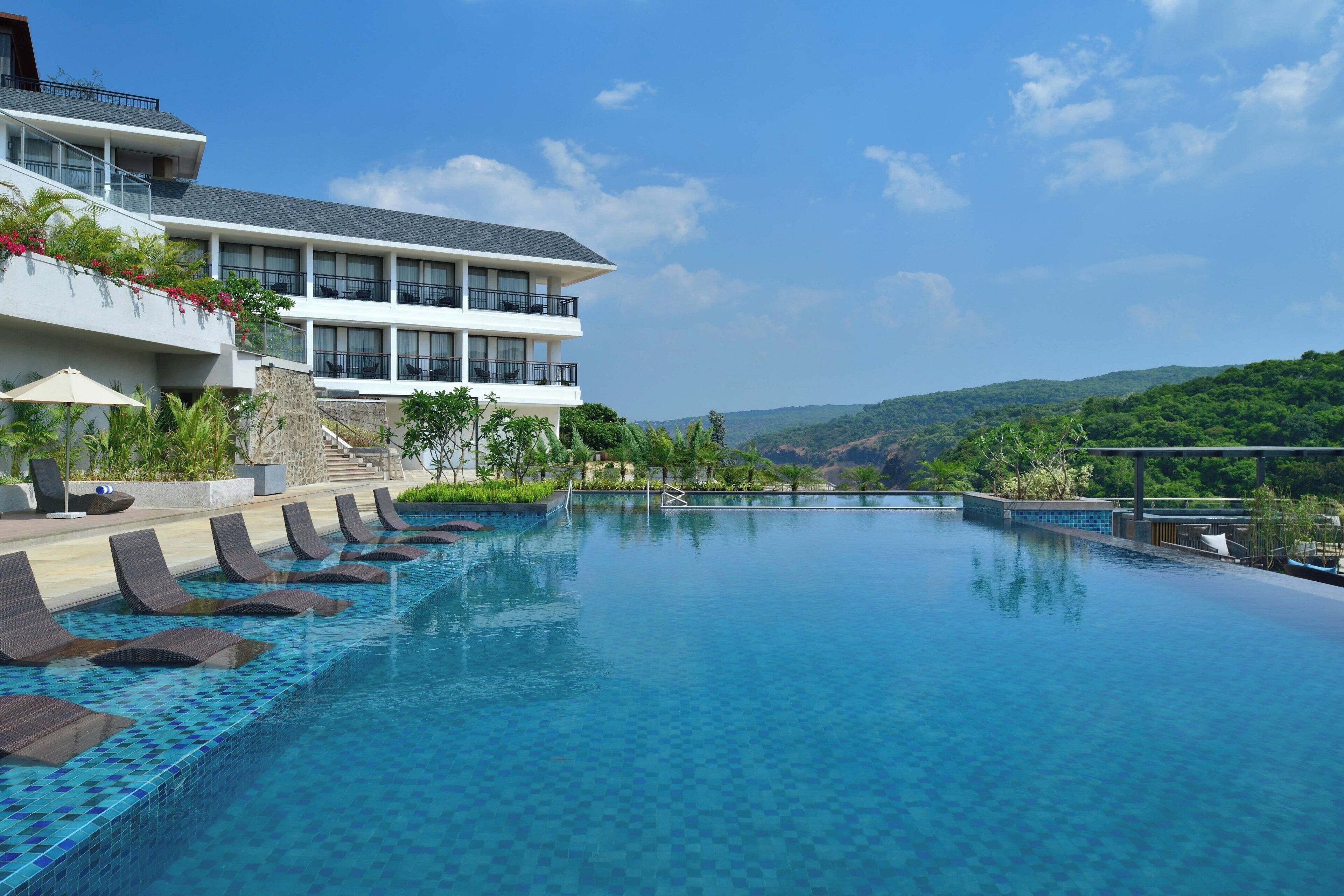 A hotel with a large infinity pool, a multi-story building, and a view of the surrounding hills.