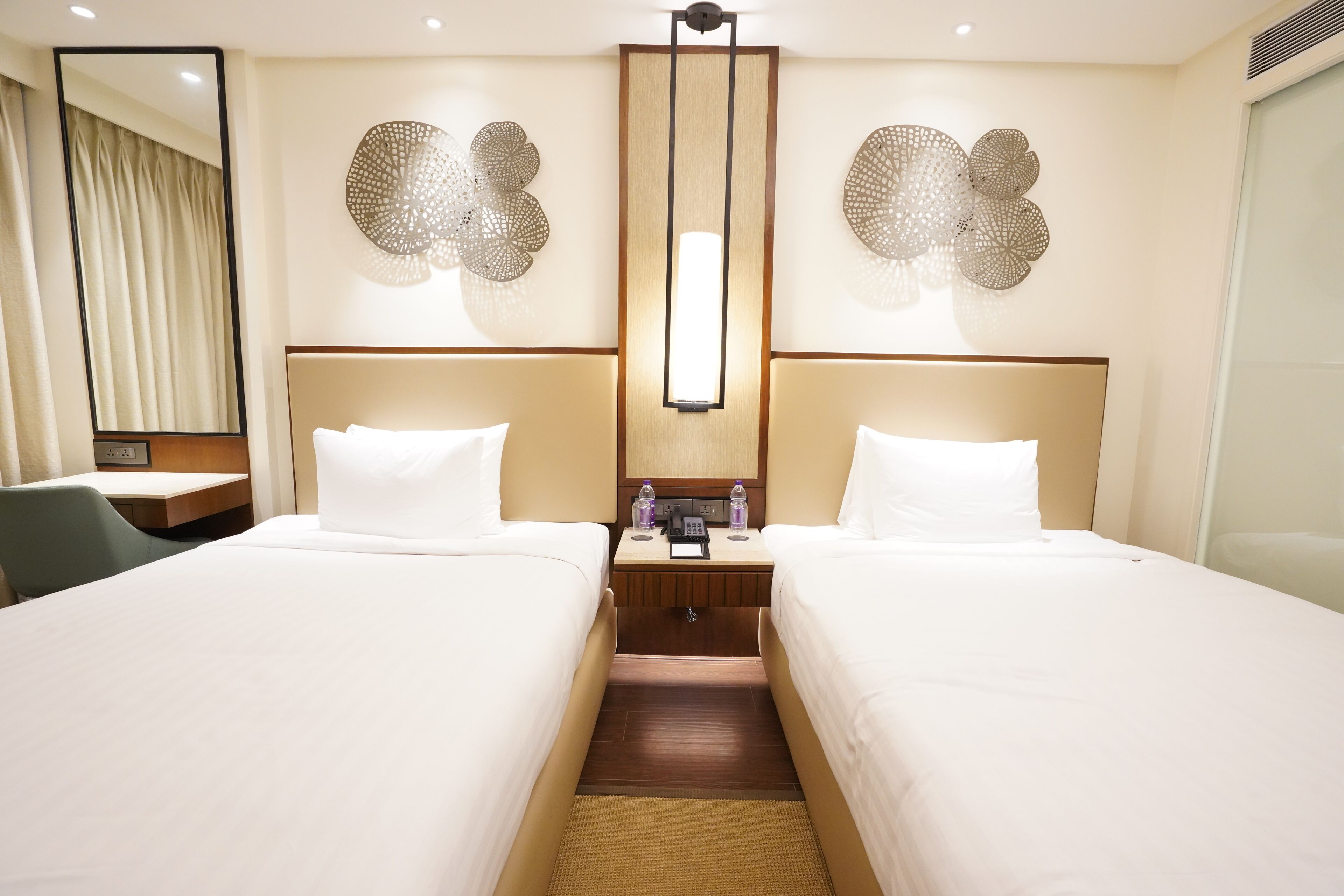 A hotel room with two beds, a desk, and a mirror.