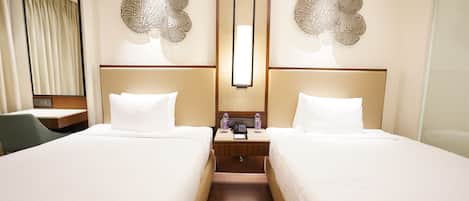 A hotel room with two beds, a desk, and a mirror.
