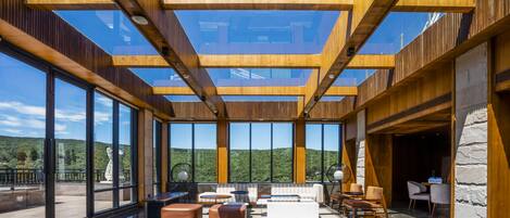 A spacious indoor area with large windows, wooden beams, and modern furniture.