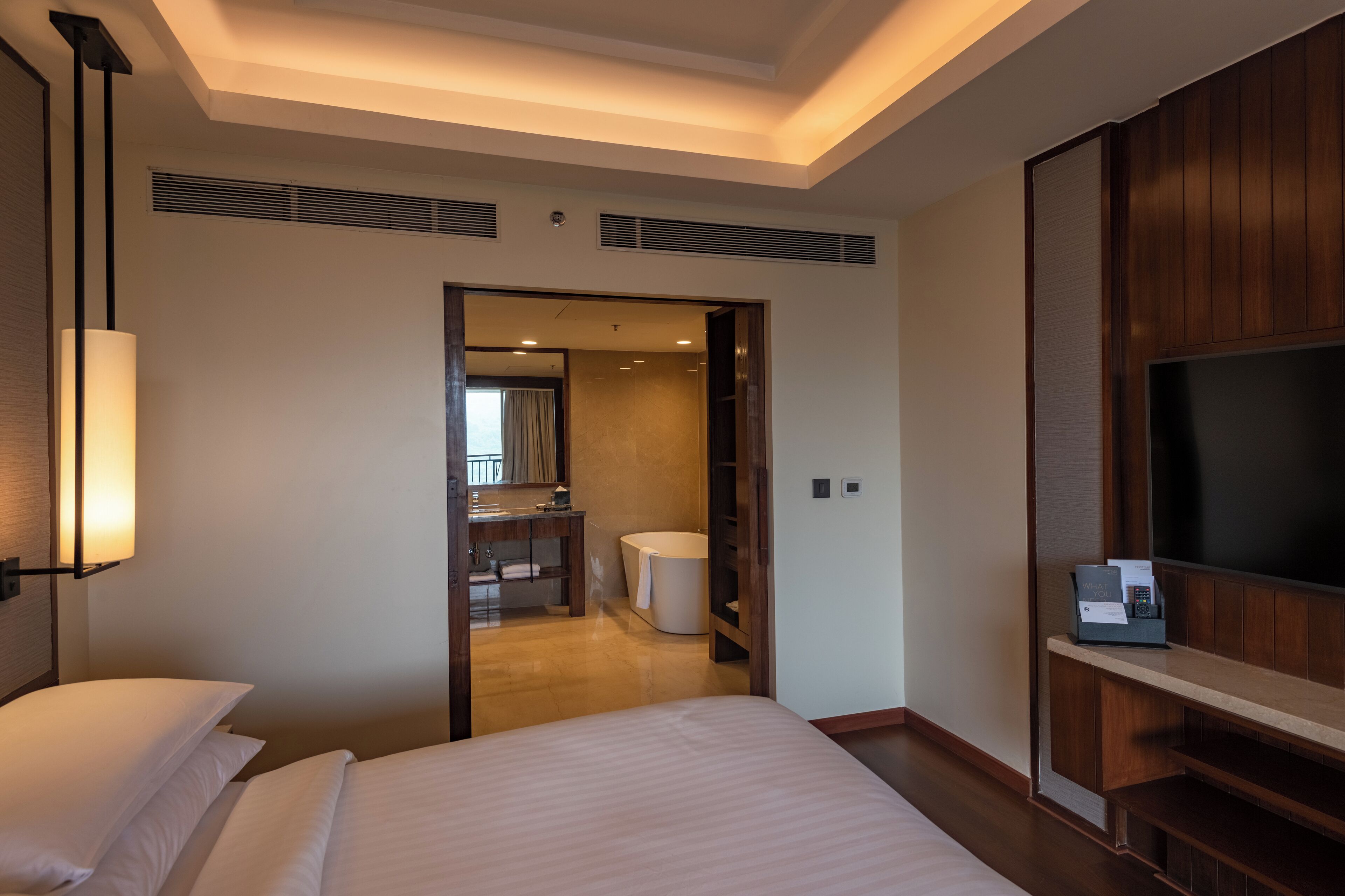 A hotel room with a bed, a TV, a desk, and a bathroom visible through an open door.