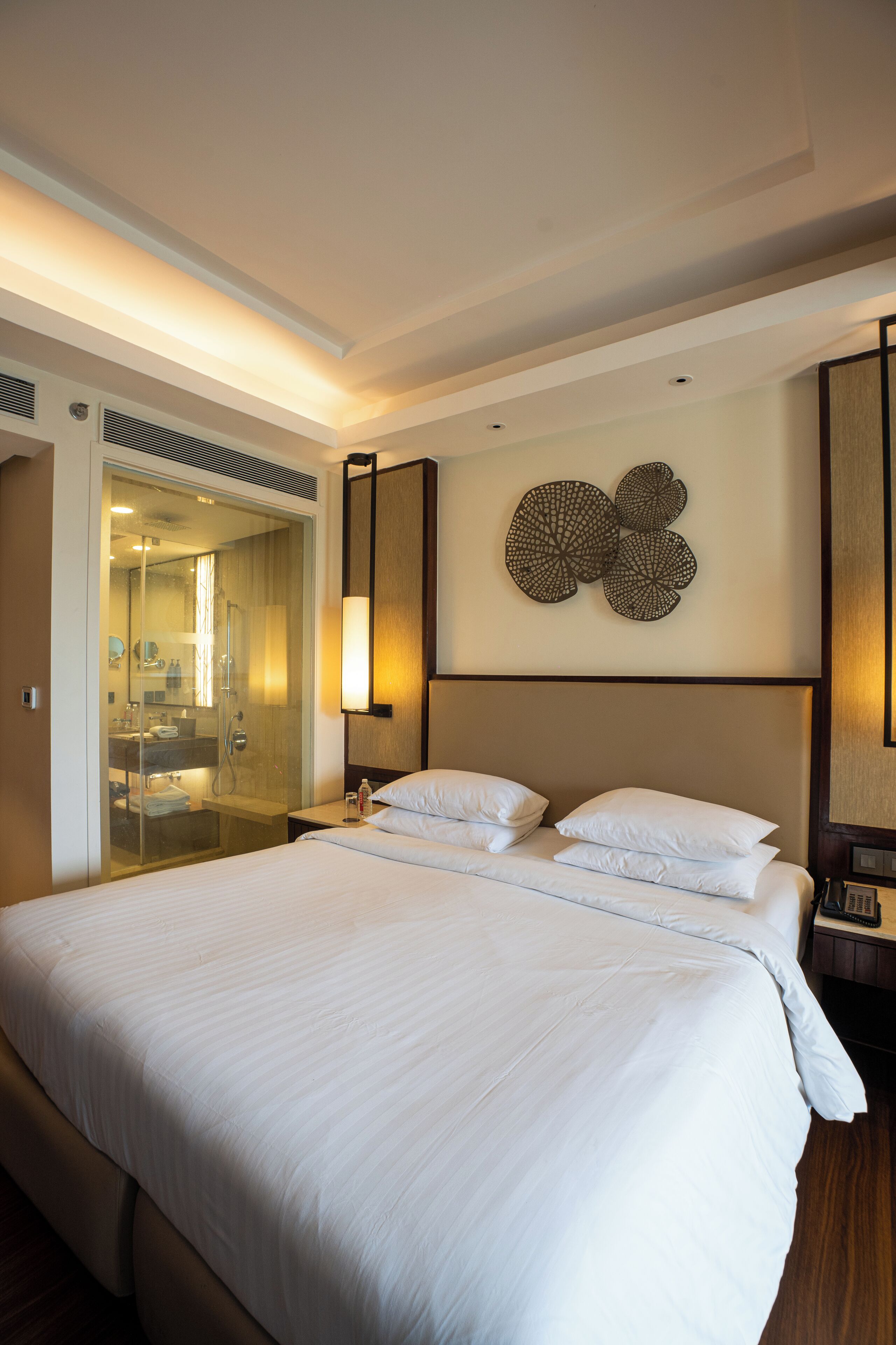 A hotel room with a large bed, a walk-in closet, a bathroom with a glass shower enclosure, and a wall-mounted decorative piece.