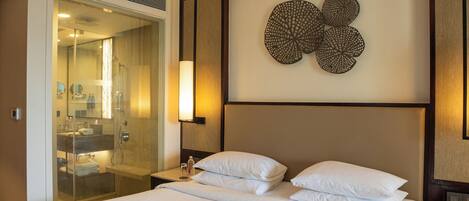 A hotel room with a large bed, a walk-in closet, a bathroom with a glass shower enclosure, and a wall-mounted decorative piece.