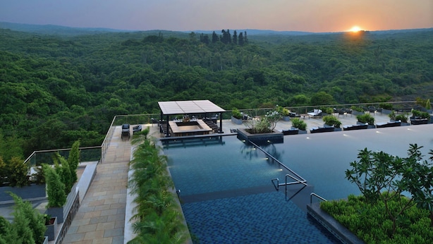 A rooftop infinity pool with a view of a forested landscape and a sunset. - Courtyard by Marriott Mahabaleshwar (Mahabaleshwar)