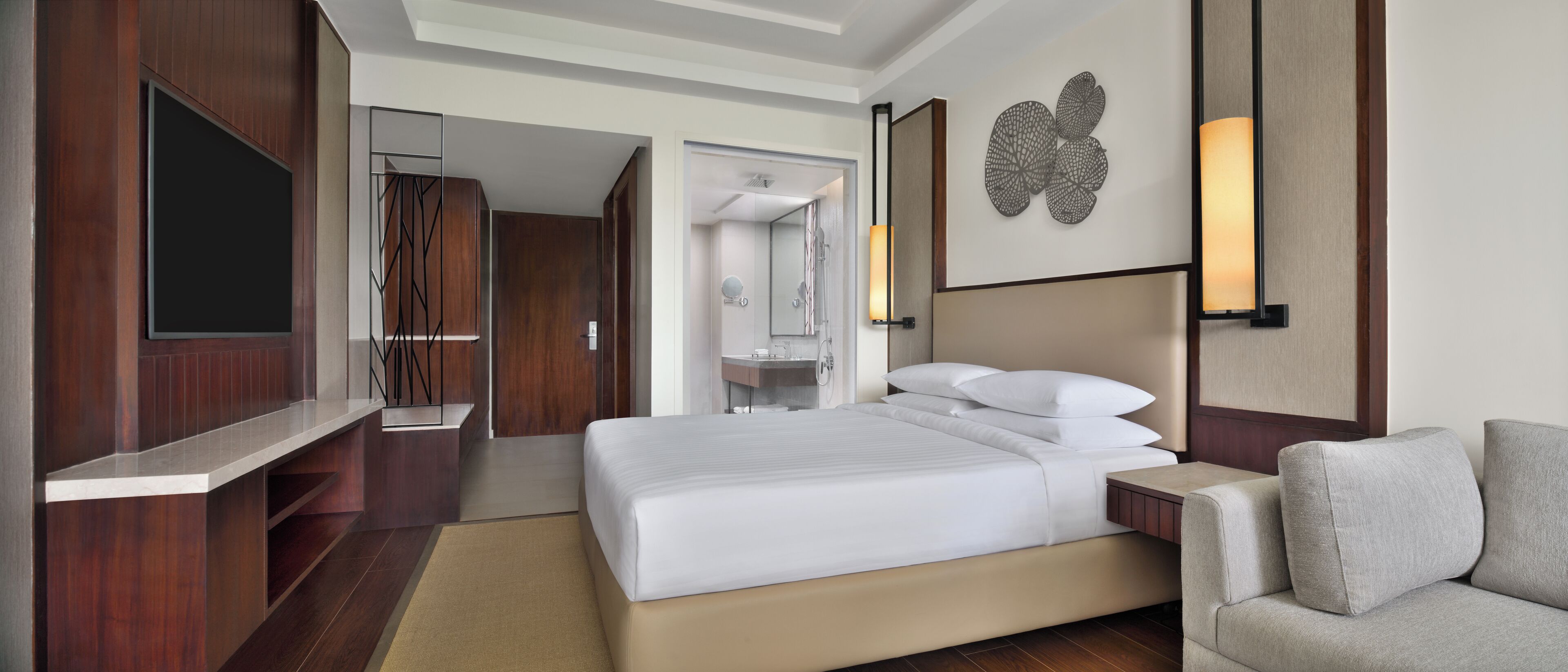 Une chambre d’hôtel moderne dotée d’un grand lit, d’un coin salon, d’une coiffeuse avec un miroir et d’une télévision.