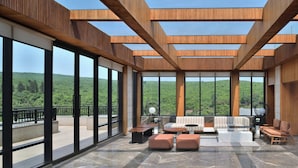 A spacious balcony with a view of green hills, modern wooden beams, and a seating area with a sofa and ottomans. - Courtyard by Marriott Mahabaleshwar (Mahabaleshwar)