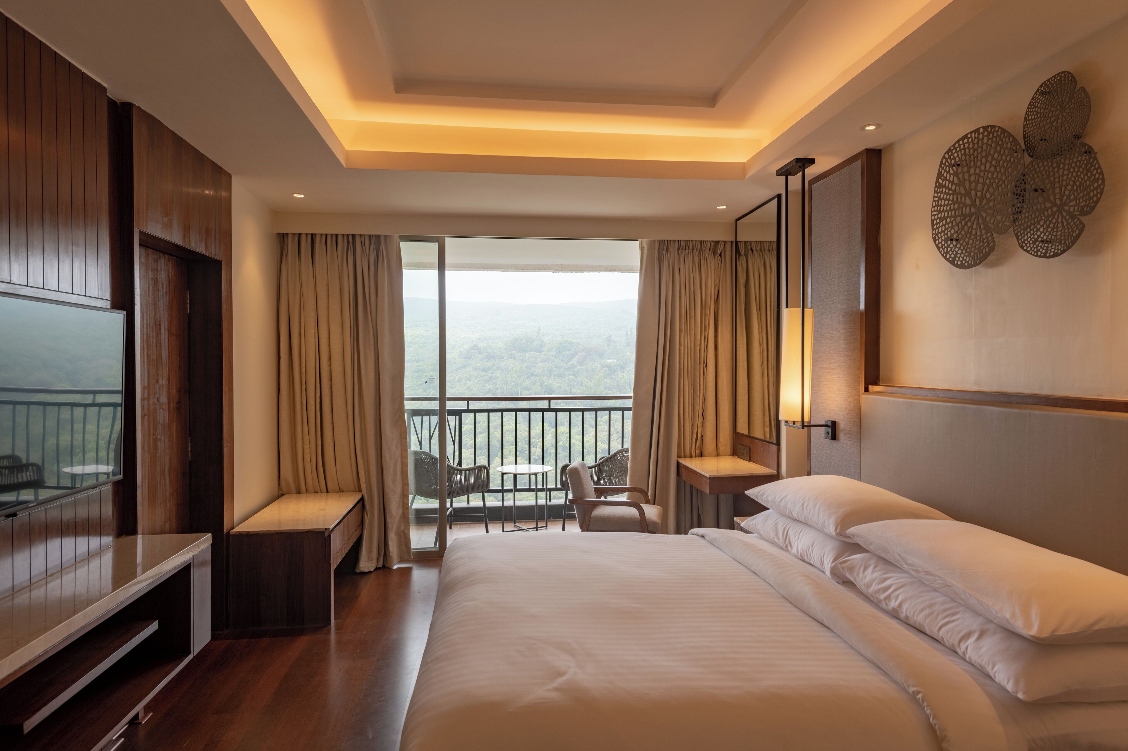 A hotel room with a large bed, a TV, a desk, and a balcony with a view.