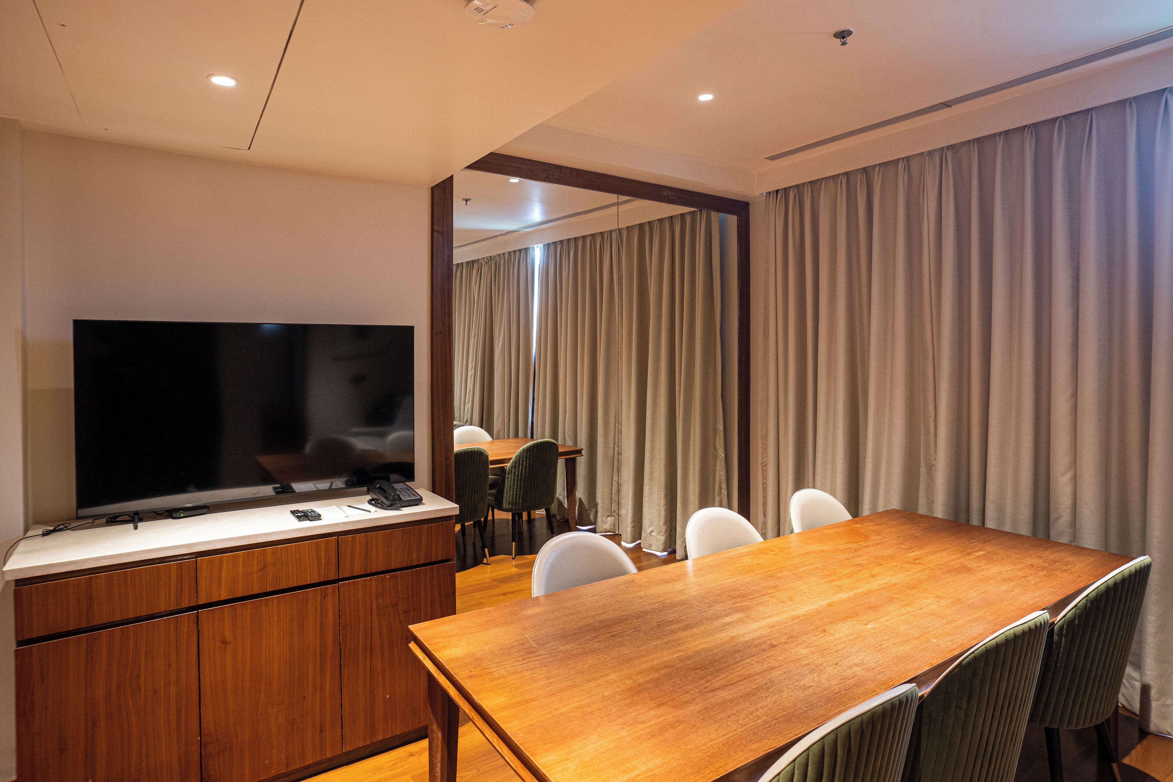 A modern conference room with a wooden table, white chairs, a large flat-screen TV, and a wooden cabinet.