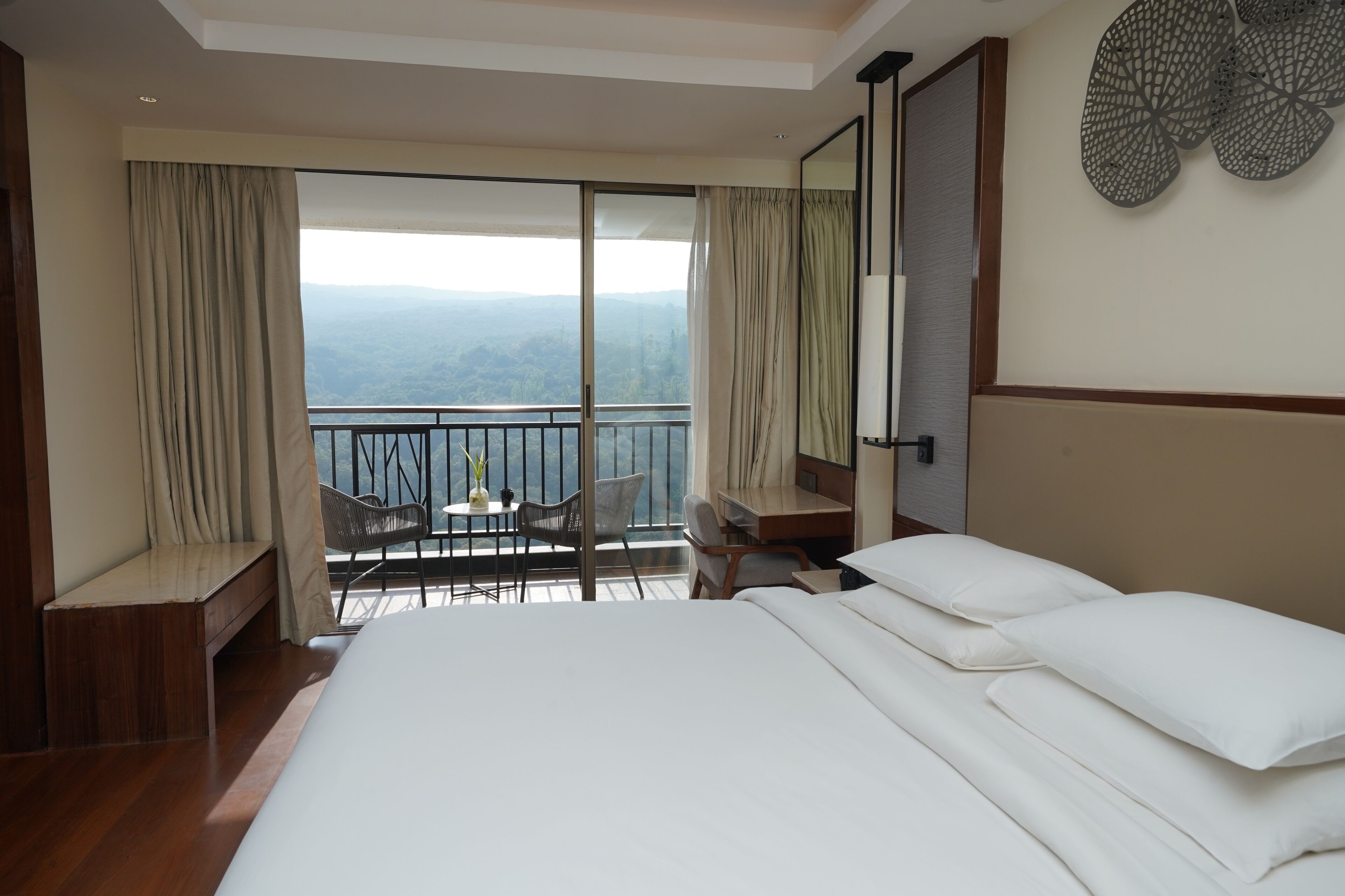 A hotel room with a large bed, a desk, and a balcony with a view of the mountains.