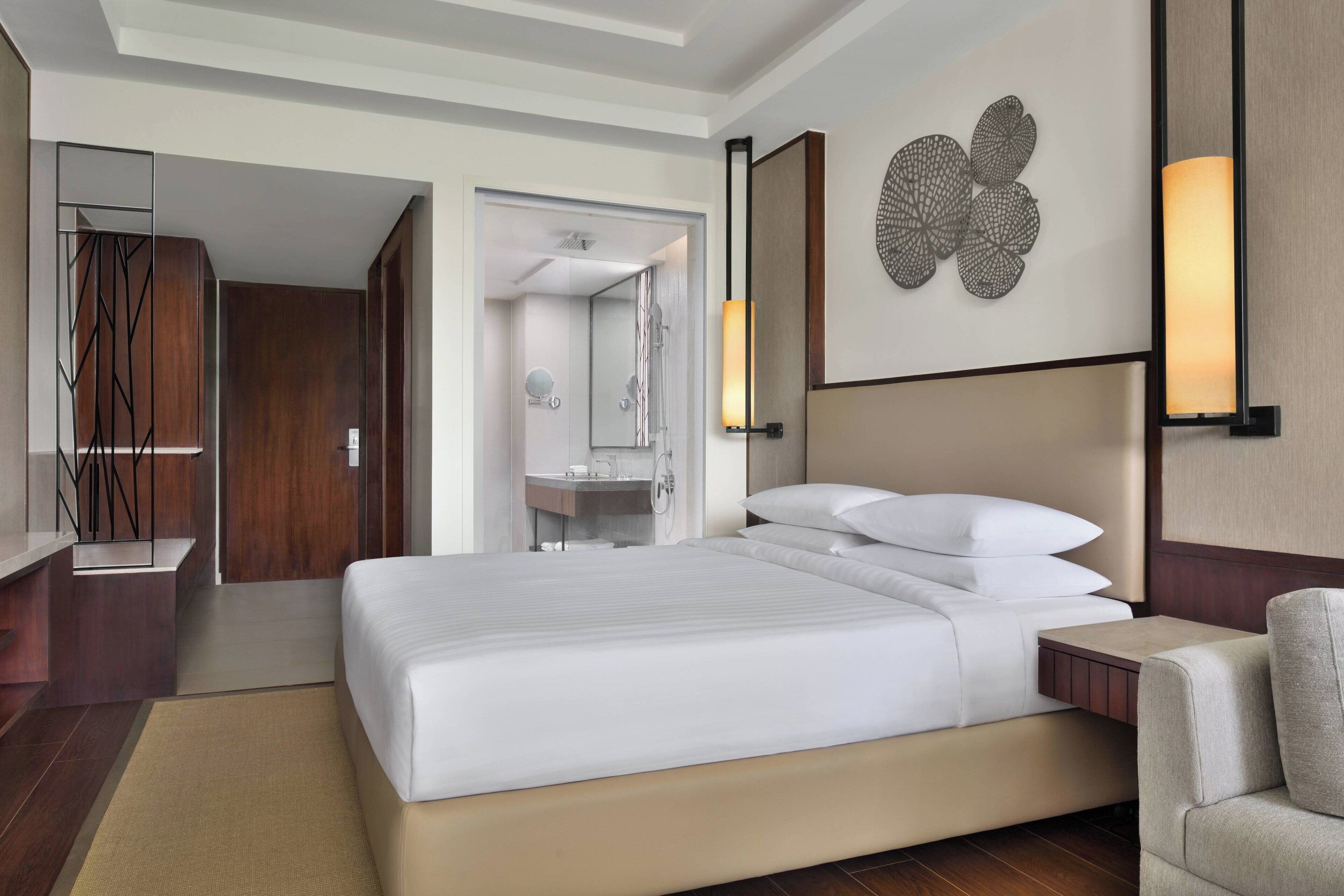 Une chambre d’hôtel moderne, dotée d’un grand lit, d’une table de chevet, d’une chaise, d’un miroir et d’un luminaire fixé au mur.