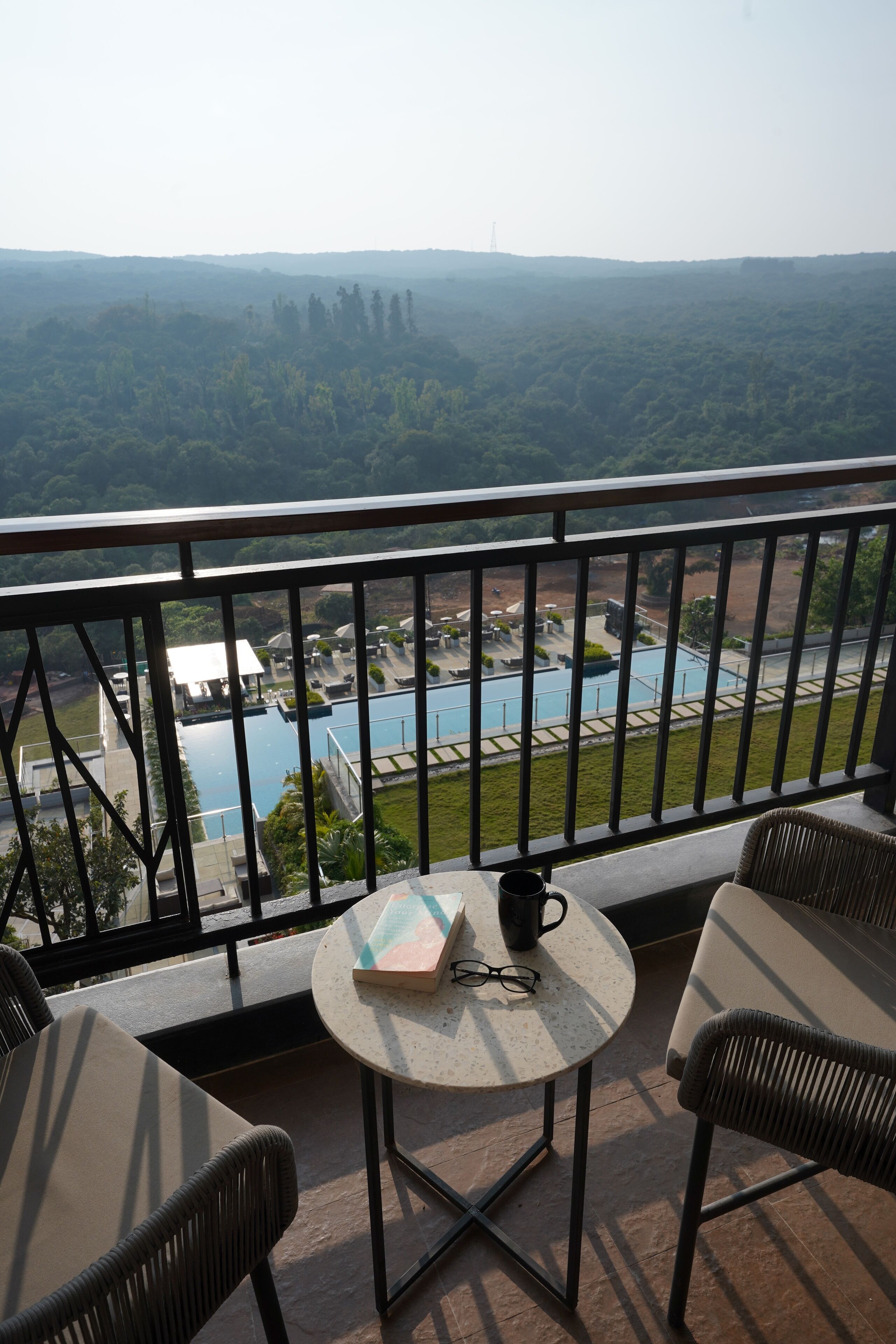 A balcony with a view of a swimming pool and surrounding landscape.