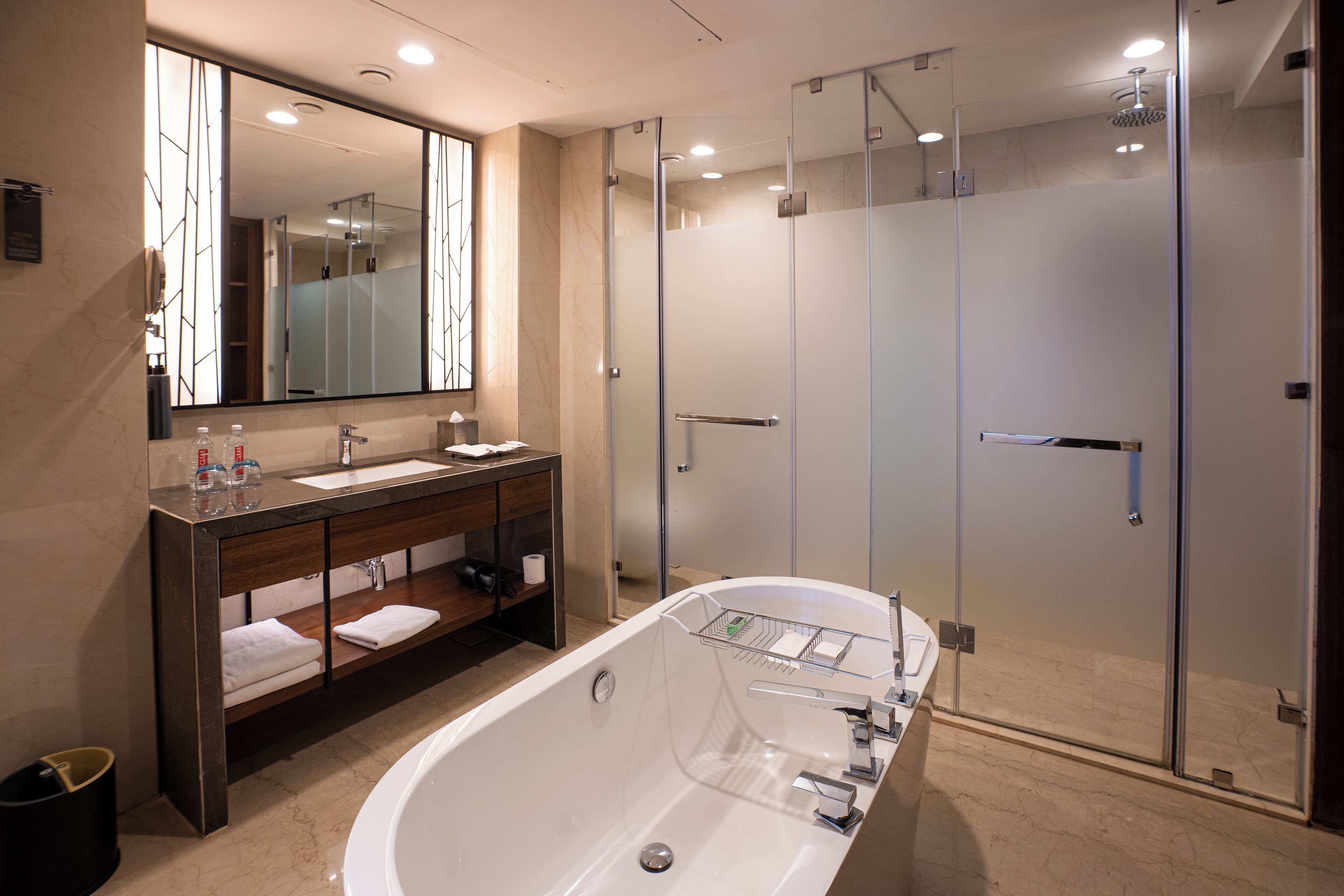 Un baño moderno con un espejo grande, una bañera, una ducha con cerramiento de vidrio y un tocador con lavamanos y toallero.