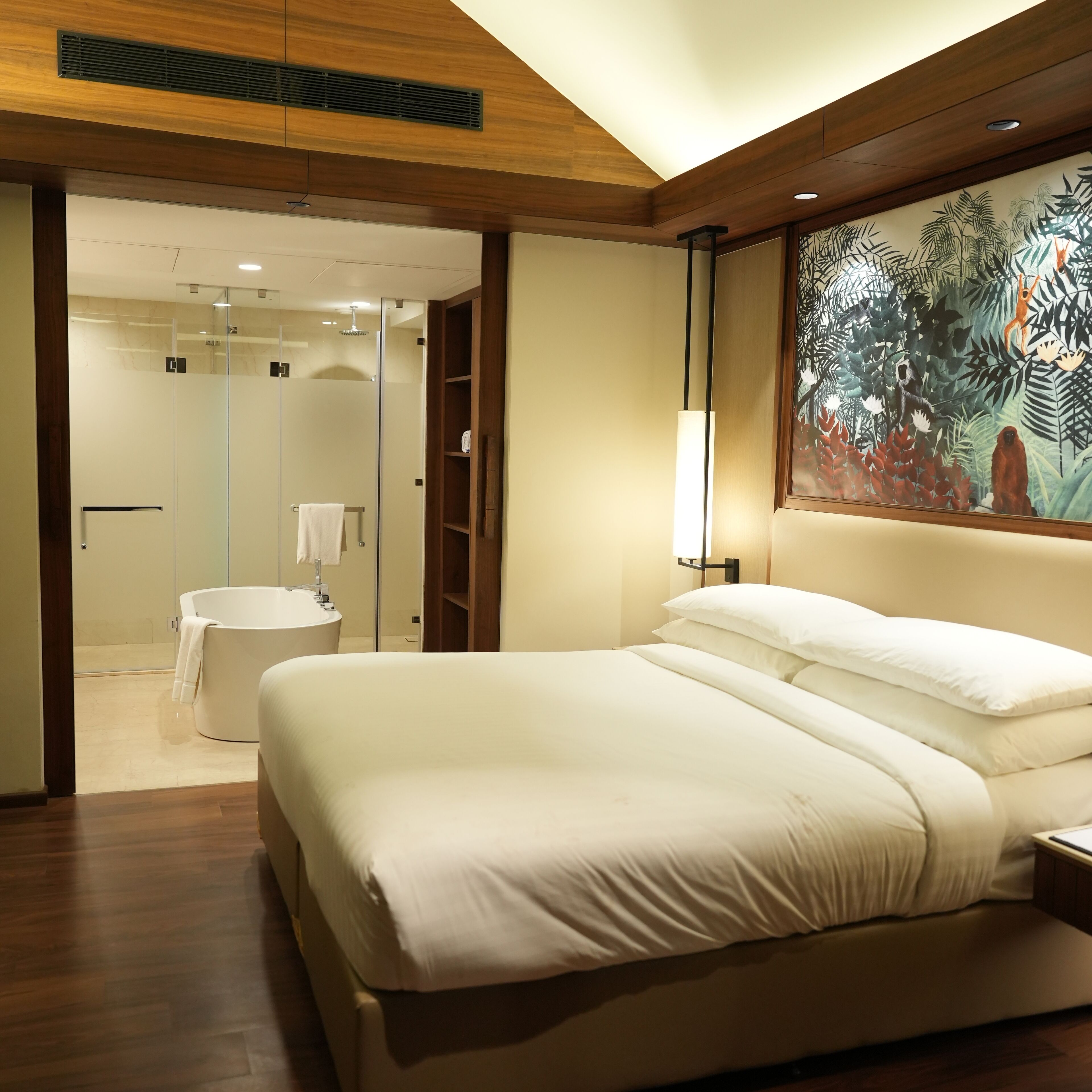 A modern bedroom with a large bed, a walk-in closet, a bathroom with a glass shower, and a large painting of a jungle scene.