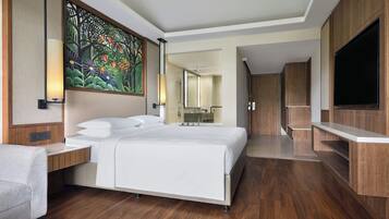 Una habitación de hotel moderna con una cama grande, suelo de madera, televisor y baño visible a través de una puerta abierta.