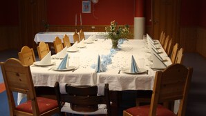 A long dining table set for a formal event, surrounded by wooden chairs with red cushions. - Dovreskogen Gjestegård  (Dovre)