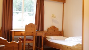 A room with a wooden bed, a desk with a chair, and a window with curtains. - Dovreskogen Gjestegård  (Dovre)