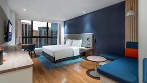 A modern hotel room with a large bed, a desk, a chair, and a sofa.
