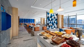 A modern hotel dining area with a buffet setup, seating arrangements, and a view of the cityscape through large windows. - Holiday Inn Express Chengdu High-Tech Zone by IHG (Chengdu)