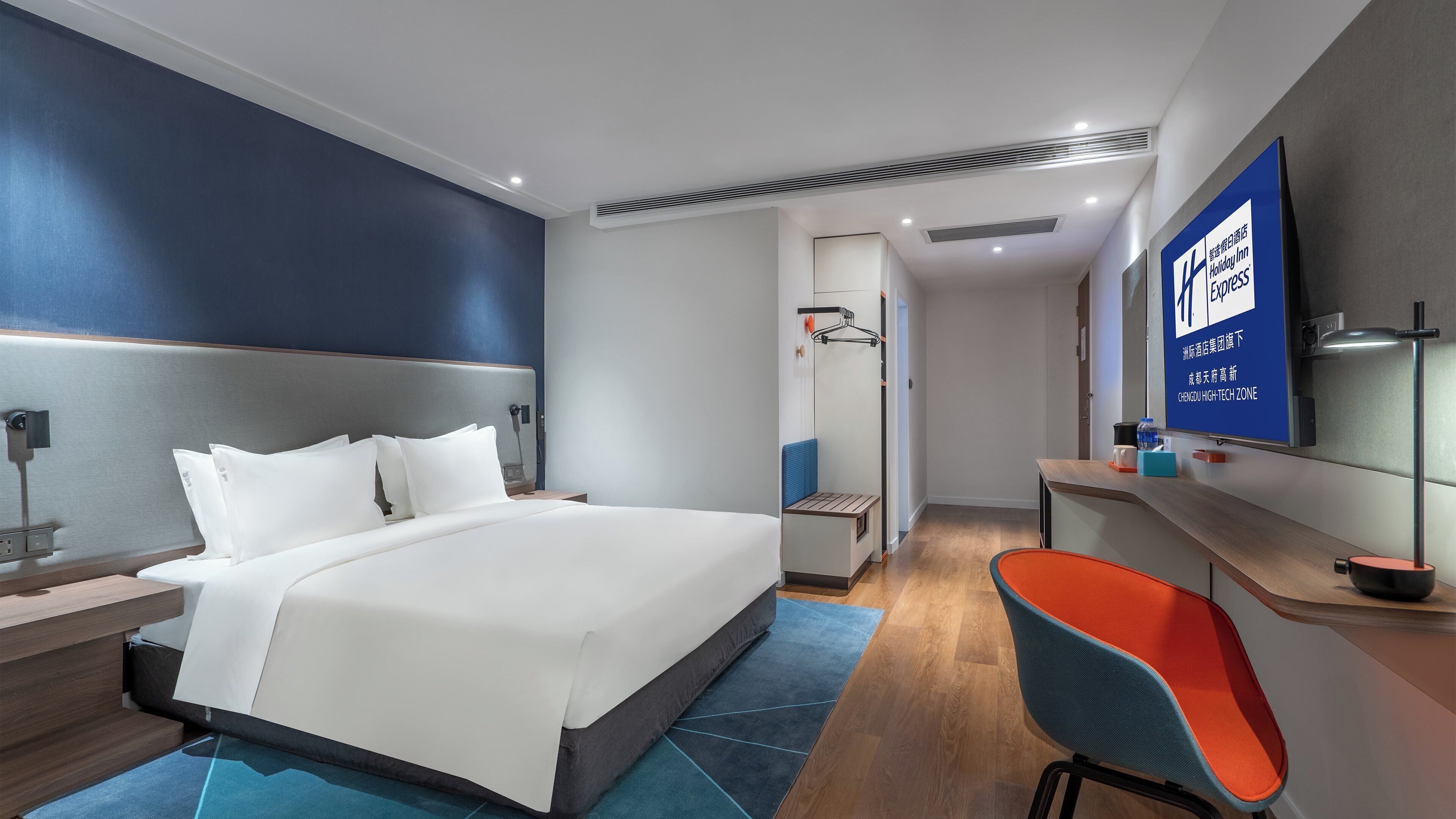 A modern hotel room with a large bed, a desk, a chair, and a flat-screen TV.