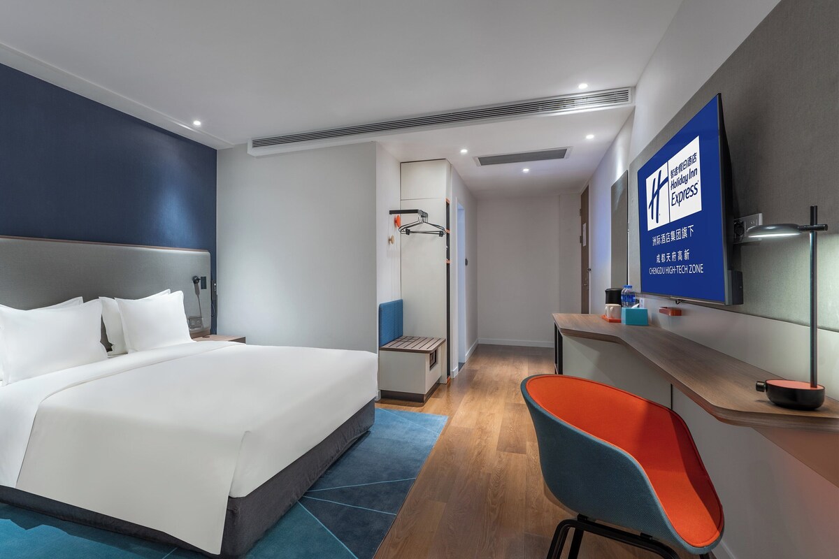 Ett modernt hotellrum med en stor säng, ett skrivbord, en stol och en tv.