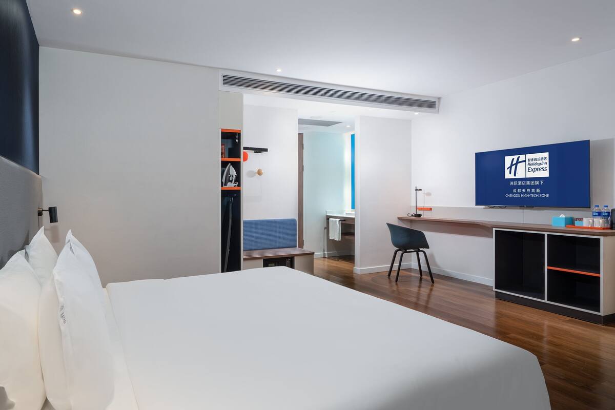 A hotel room with a bed, a desk, a chair, and a television displaying the Holiday Inn Express logo.