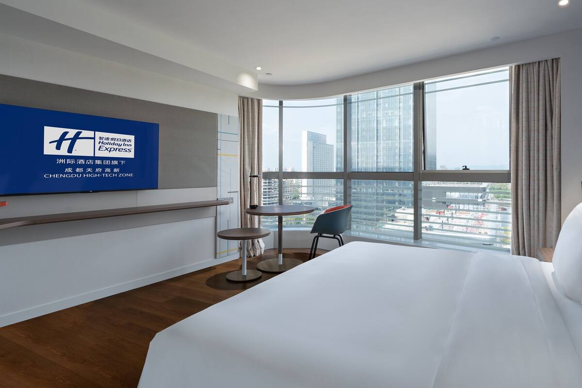 A hotel room with a large bed, a desk, and a view of the cityscape.