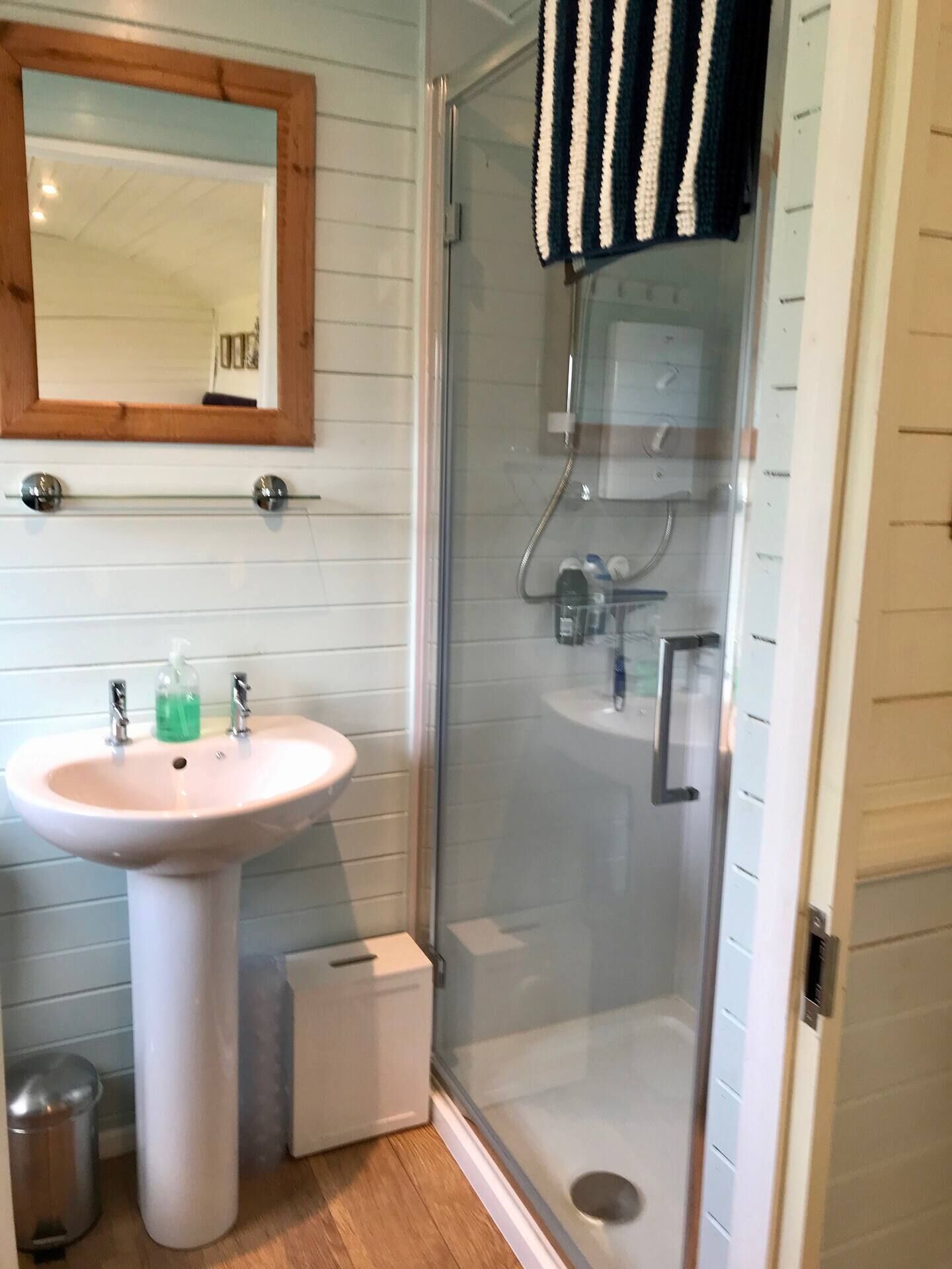 A bathroom with a white pedestal sink, a glass shower enclosure, and a wooden-framed mirror.