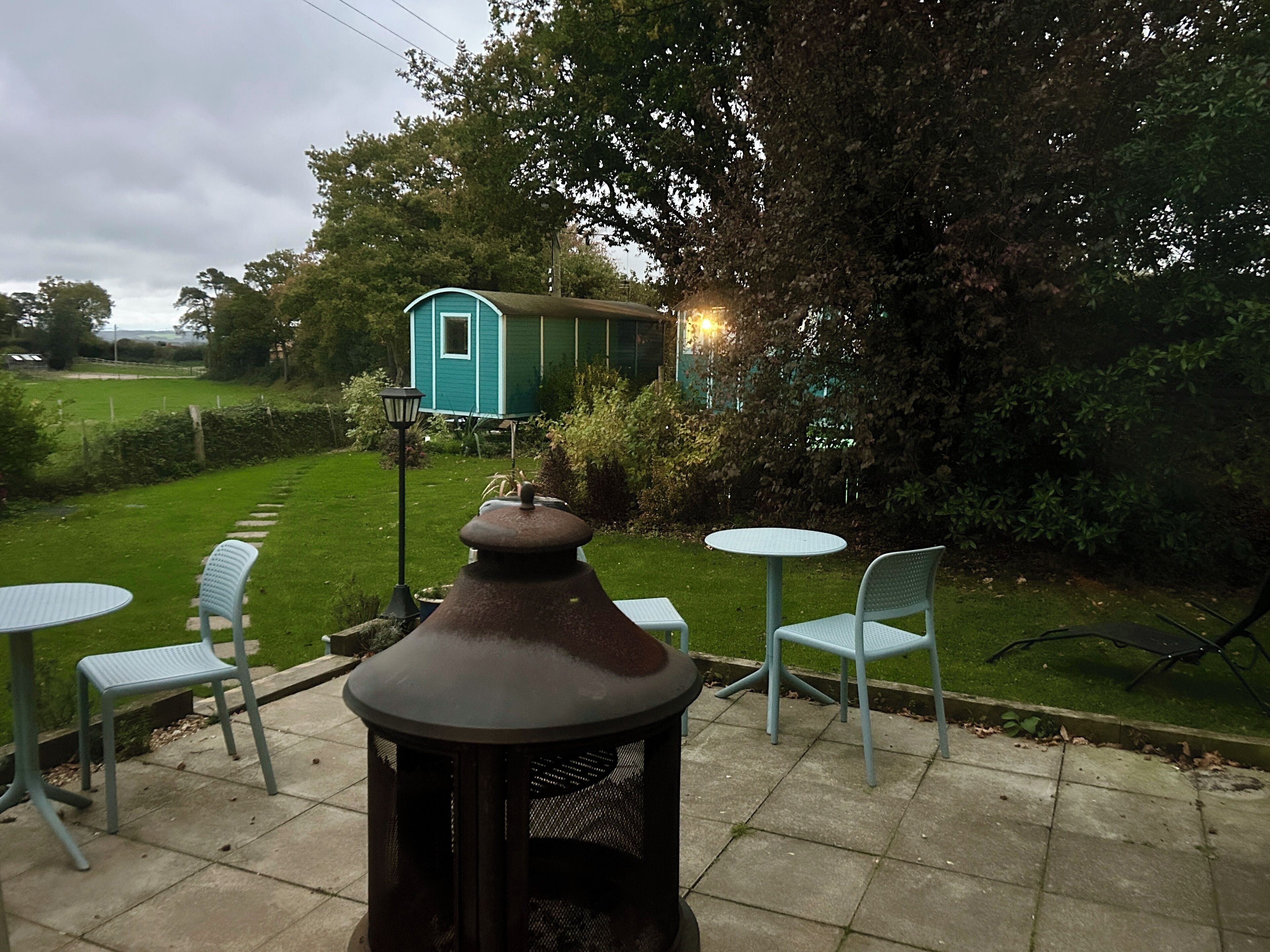 A patio with a metal table and chairs, a decorative chimney, and a small blue house in the background.