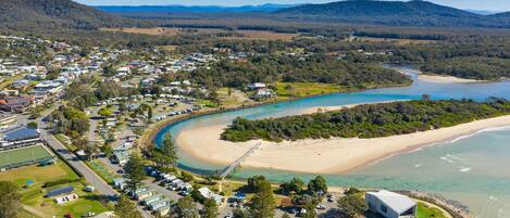A coastal area with a beach, a river, and a residential zone with houses and parked vehicles.