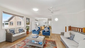 A modern living room with a sofa, armchairs, a coffee table, and a dining area in the background.