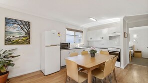 A modern kitchen with white cabinets, a microwave, and a stove. There is a dining table with chairs and a potted plant.