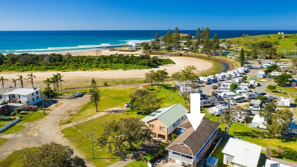 A coastal residential area with a beach, mobile homes, and a large house with a green roof.
