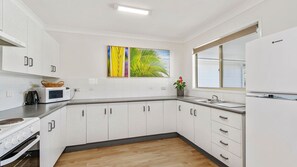 Een moderne keuken met witte kastjes, een magnetron, een fornuis, een spoelbak en een raam.