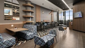 Un café moderno con asientos estampados, una barra y una gran pantalla de televisión.