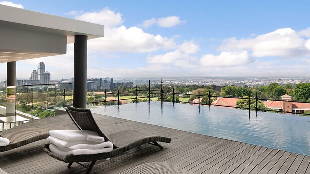 Una piscina infinita con sillones de descanso y vista a la ciudad.