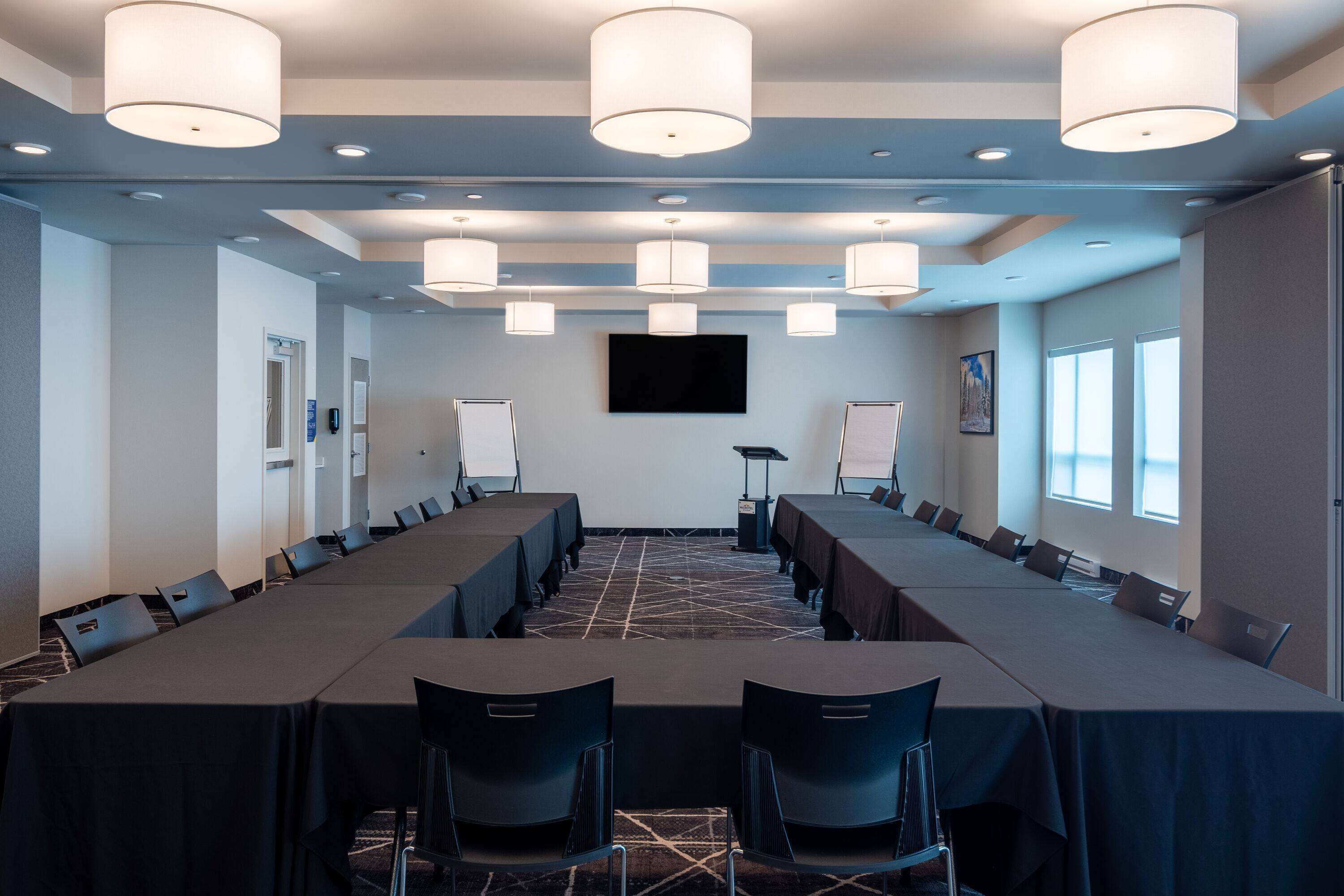 A conference room with long tables, chairs, and a large screen.