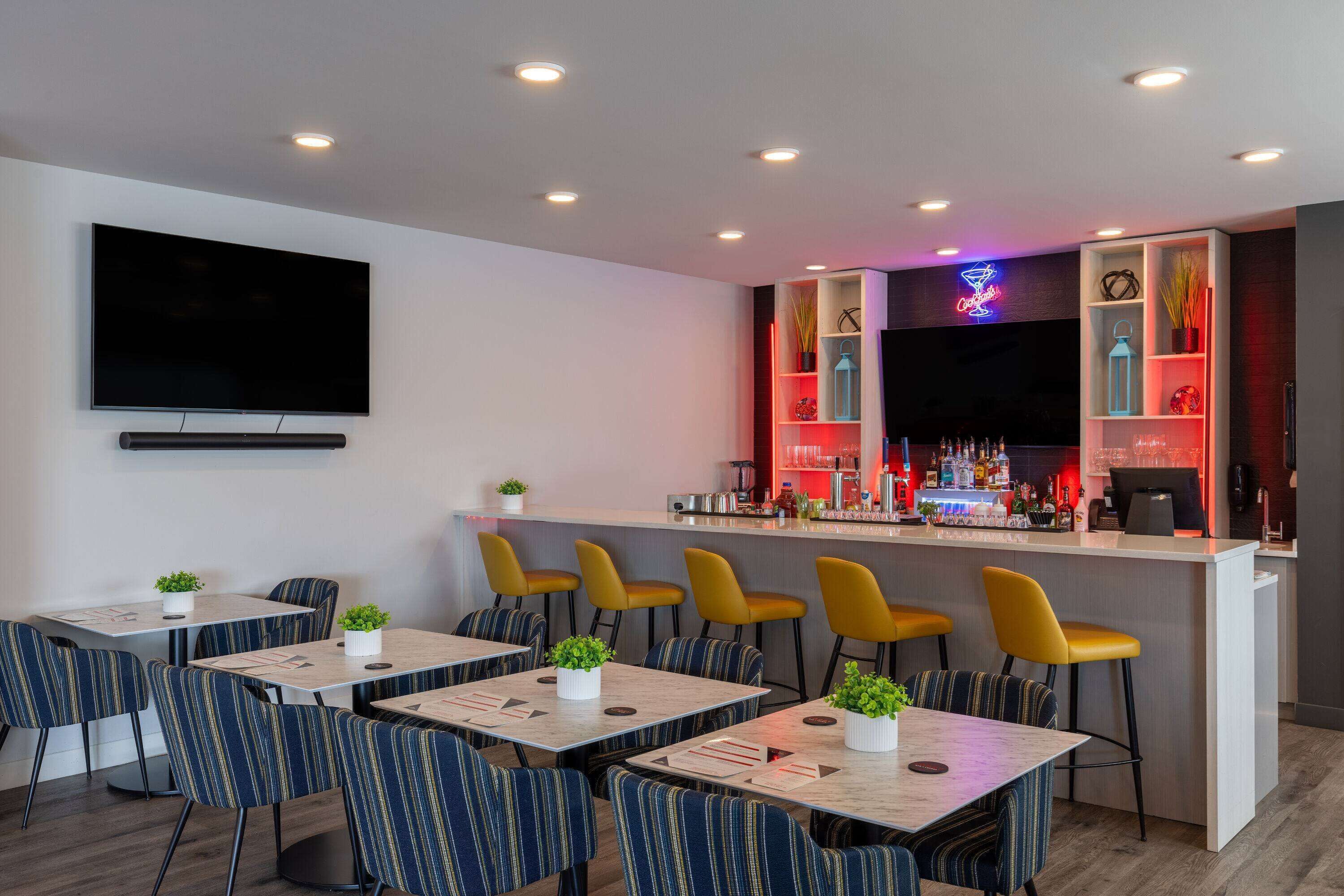 A modern bar area with a flat-screen TV, bar counter, and seating with striped chairs.