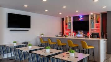 A modern bar area with a flat-screen TV, bar counter, and seating with striped chairs.