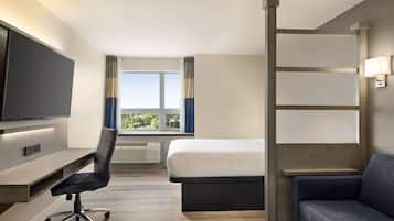 Habitación de hotel con cama, escritorio, silla, televisor, ventana con cortinas y sofá.