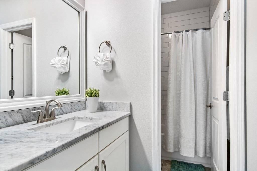 A bathroom with a marble sink, a mirror, a potted plant, and a shower curtain.